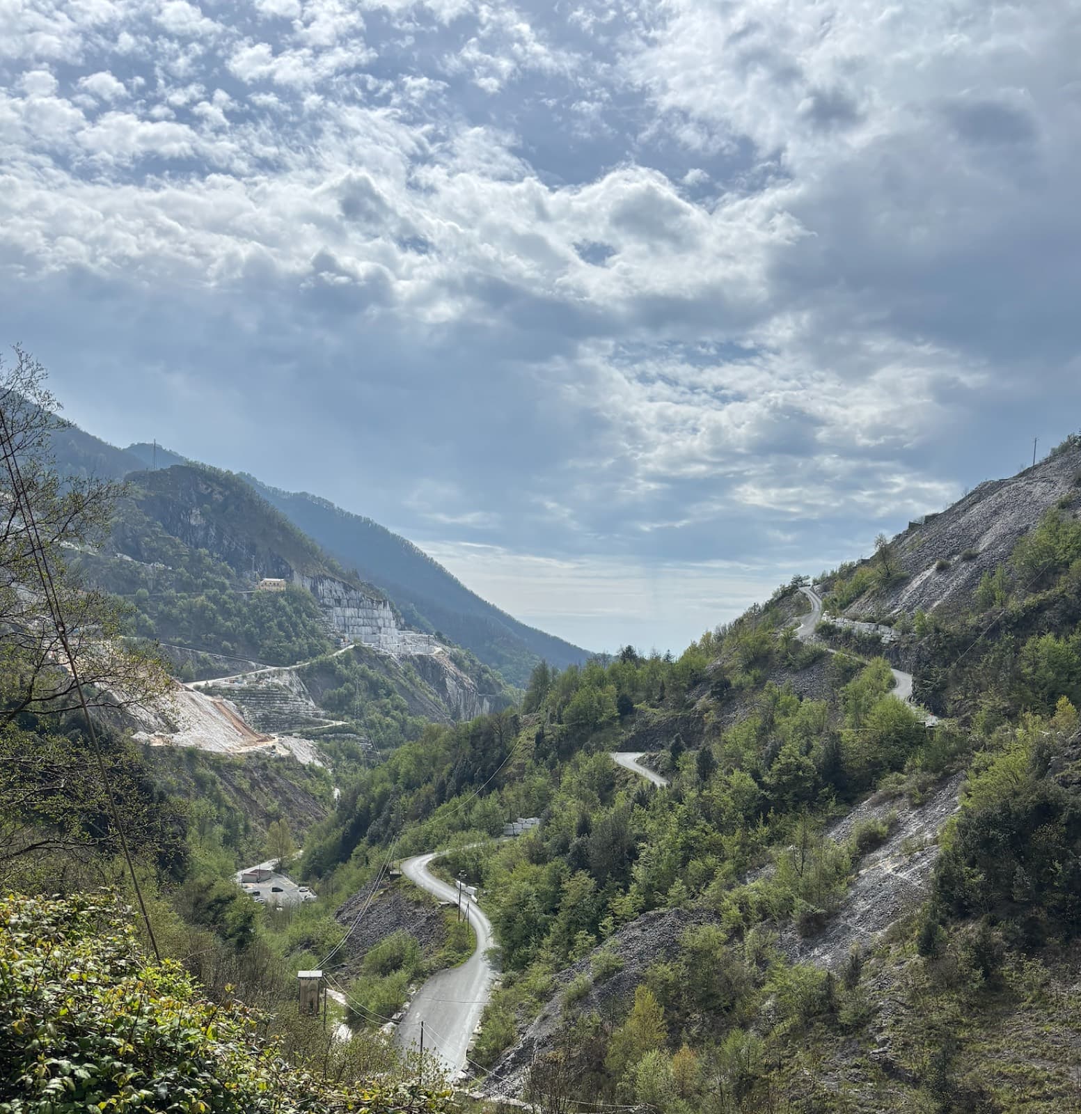 A single-track road switchbacking down a quarried valley between wooded slopes