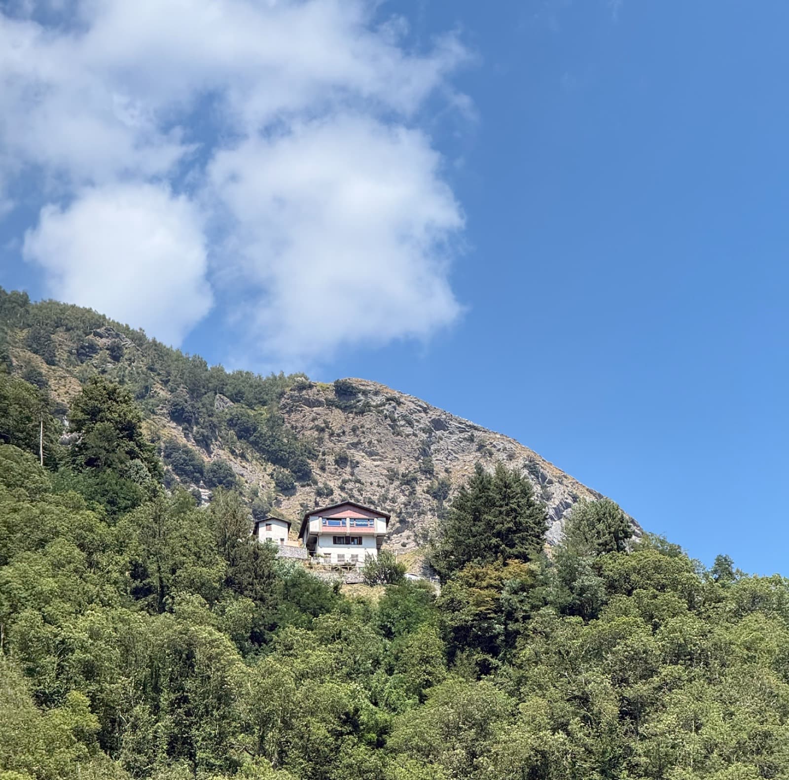 A house standing alone on a wooded shoulder below a rock outcrop