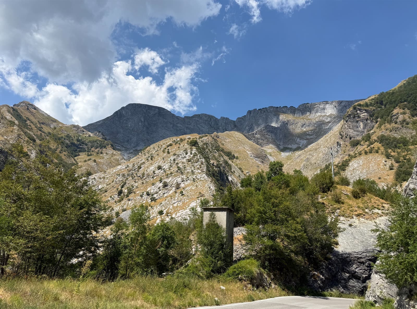 The bare crest of the Apuan Alps above green slopes, from the road over the top