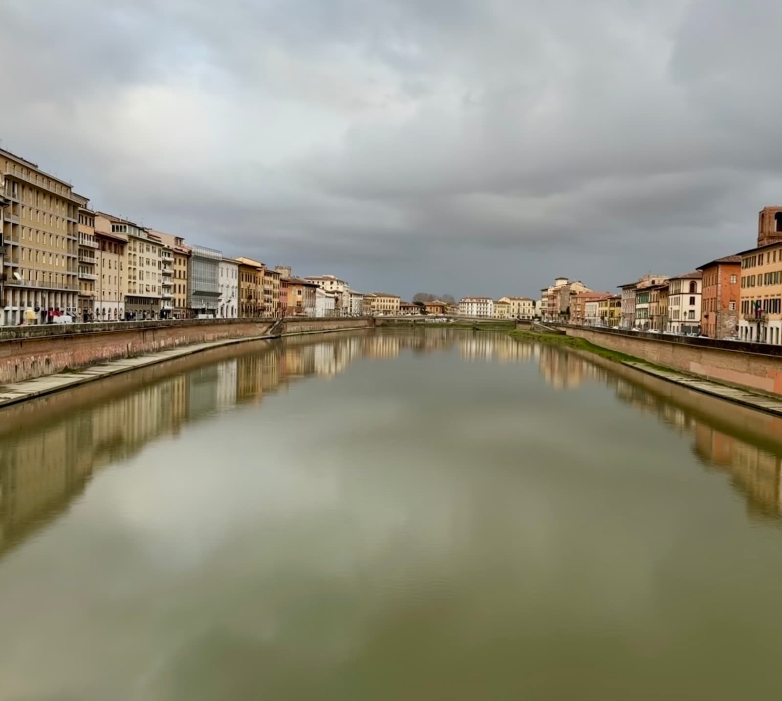 The Arno running flat and green-grey between the Lungarni under cloud