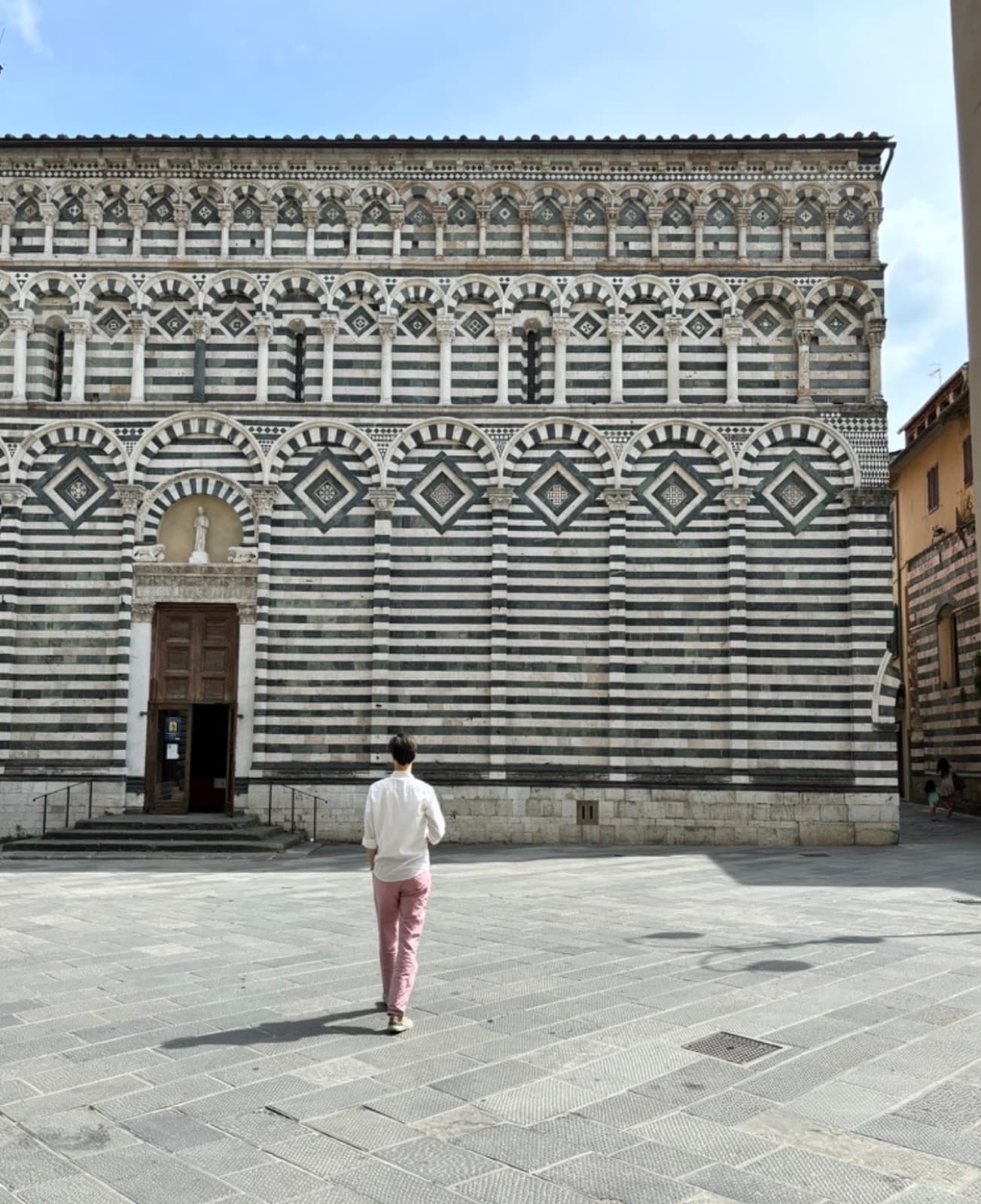 The green and white striped flank of a church at Pistoia across an empty square