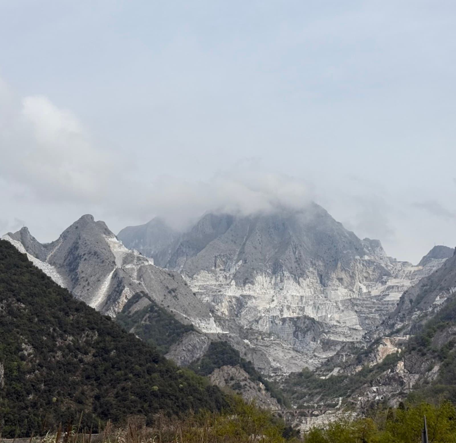 White marble quarries cut in terraces into a grey mountain, cloud sitting on the summit