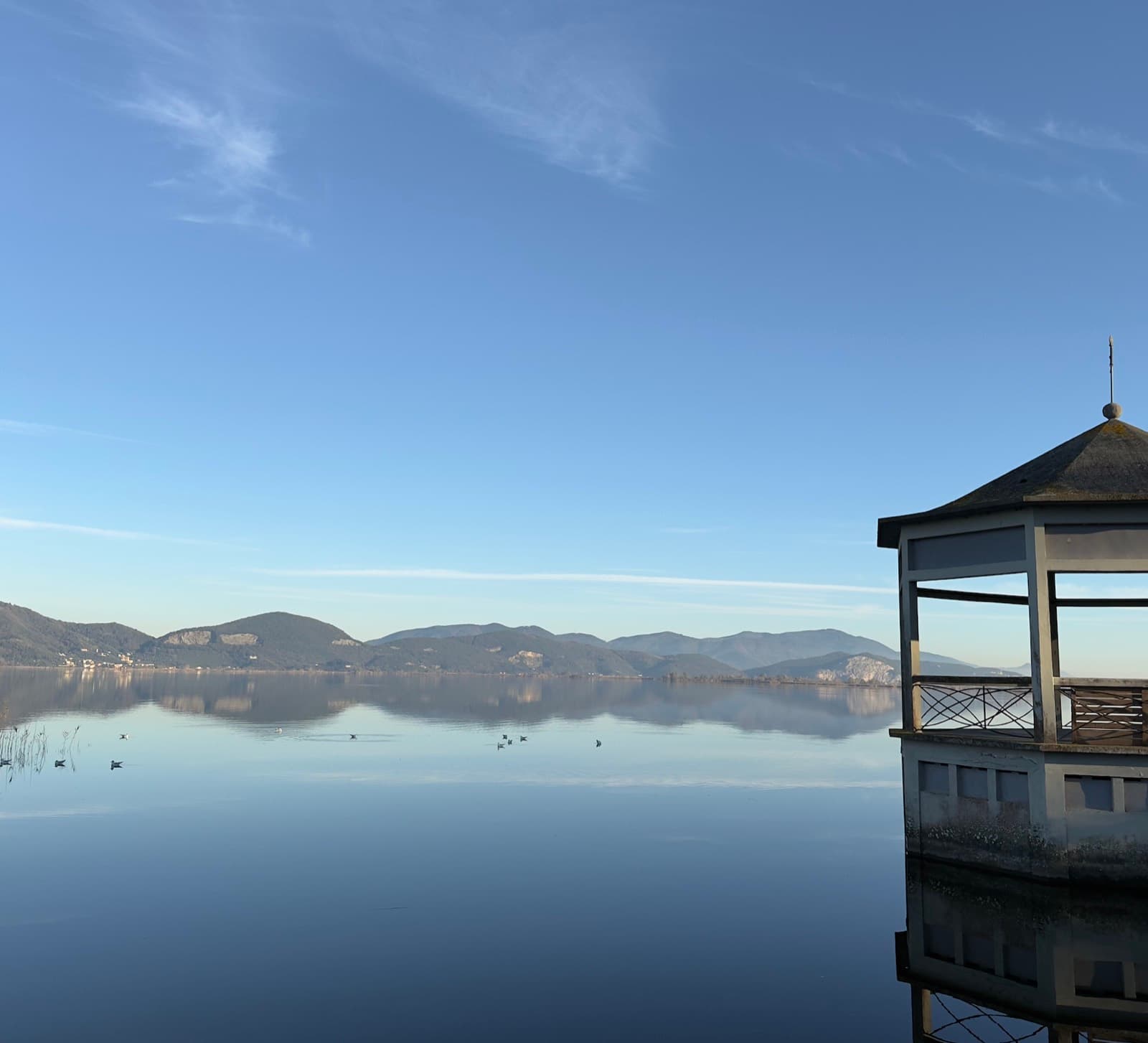 A still lake reflecting hills and sky, with a wooden pavilion at the water's edge