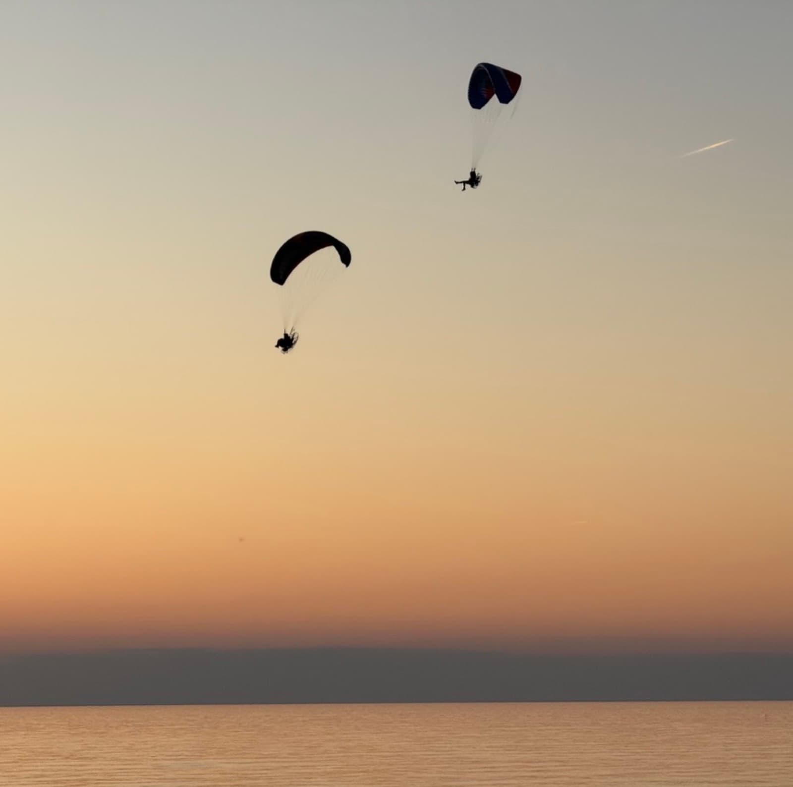 Two paramotors over a flat sea at sunset