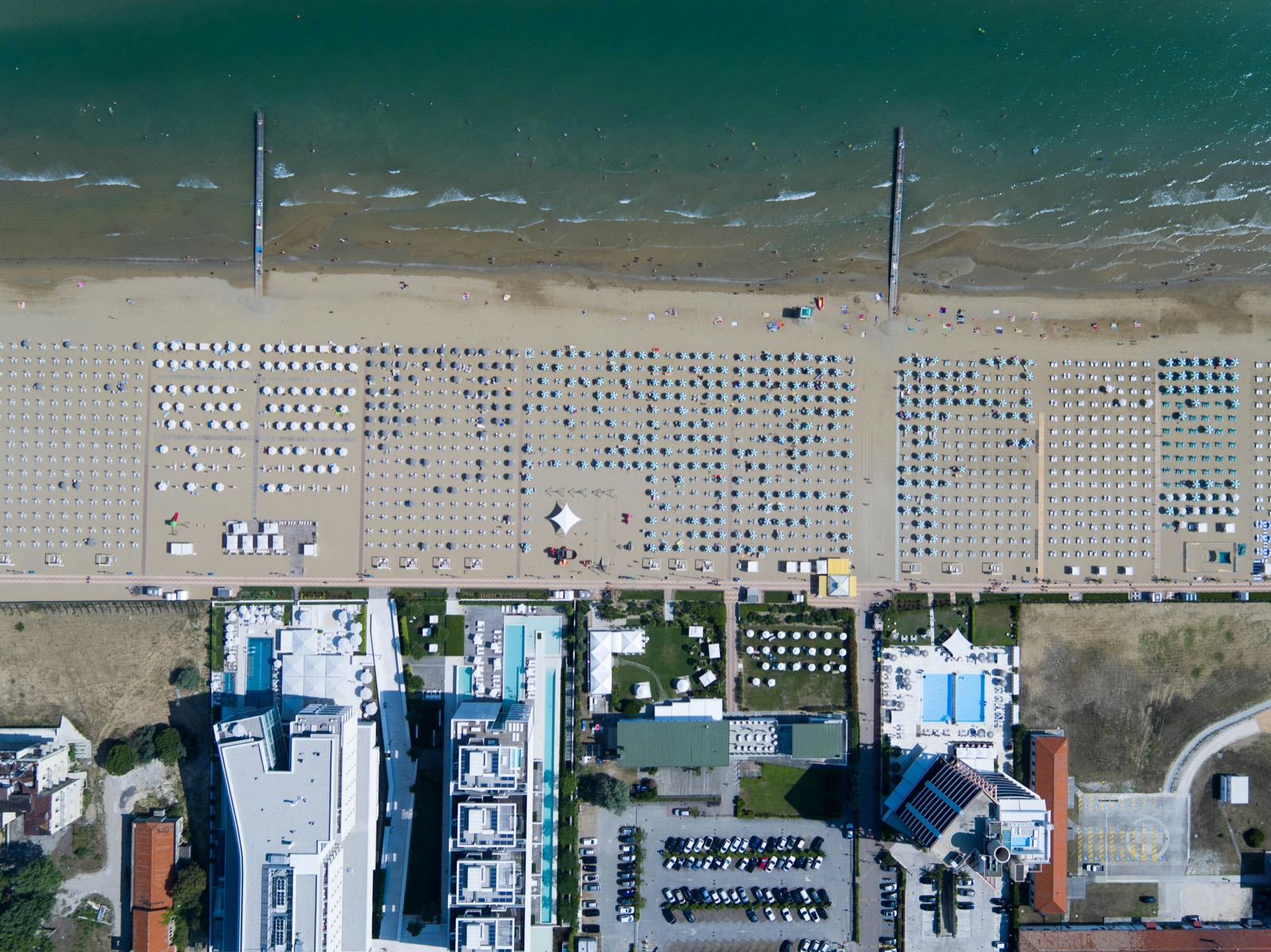 Rows of rented umbrellas in ruled blocks, and the strip of open sand at the waterline that no concession can enclose.