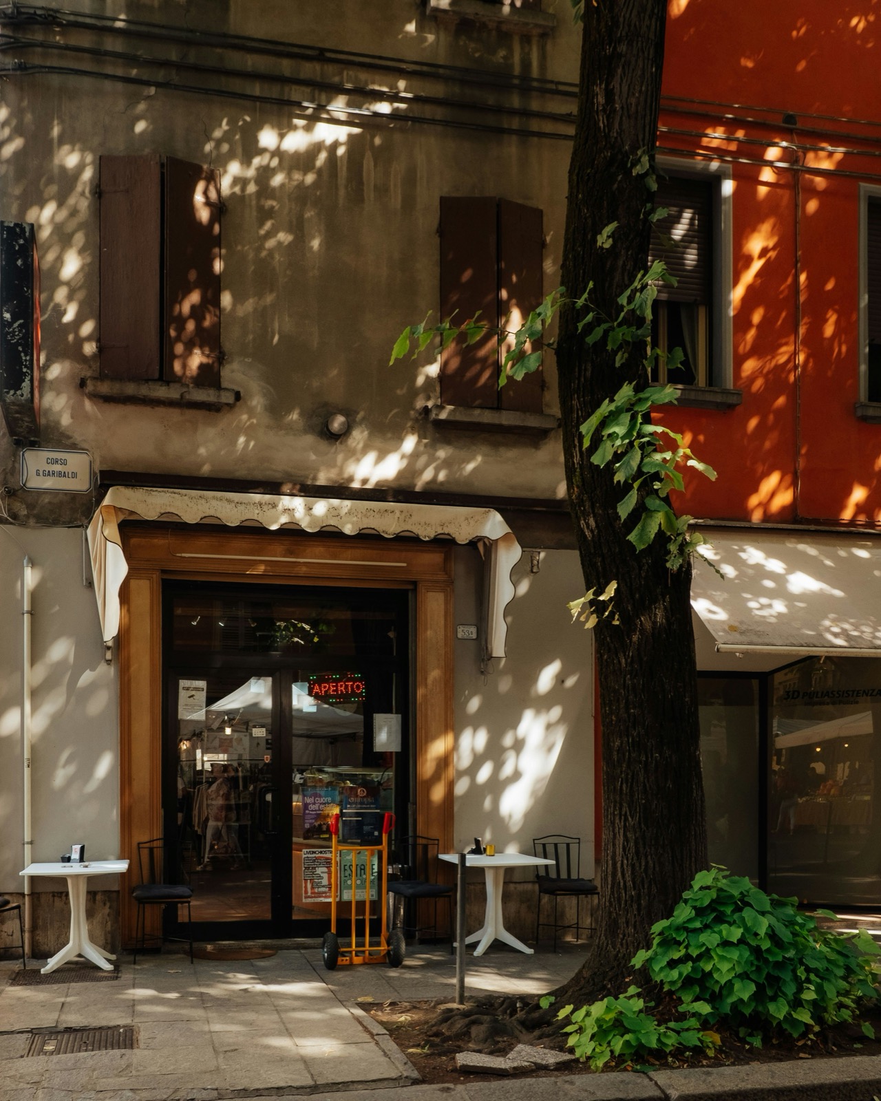 The whole institution: two tables, a doorway, and an APERTO sign, on a street that uses it from seven in the morning.